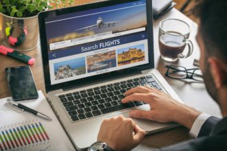 Man working with a computer, search flights on the screen, office business background.